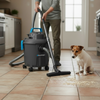 Person using a vacuum cleaner on a tiled floor with a dog watching.