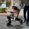 Child riding a 3-in-1 tricycle with an adult nearby, on a street.