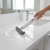 Person cleaning a white countertop with a squeegee tool in a bathroom setting.