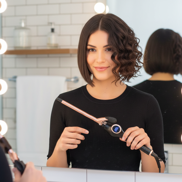 Woman styling her hair with a hair straightener in front of a mirror.