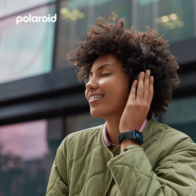 Woman wearing headphones with a blurred urban background, featuring the Polaroid logo.