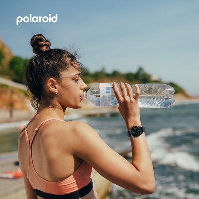 Woman drinking water by the beach wearing the Polaroid PA88 Watch.