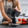 A person in a kitchen holds a black smartphone on a black adjustable stand. The stand has a text overlay that reads '90° Tilt Support' and 'Provides greater flexibility when framing your shot.