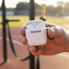 Hand holding a white case with 'Polaroid' branding, containing wireless earbuds, outdoors.