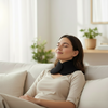 Woman relaxing on a couch with a neck pillow in a bright living room.