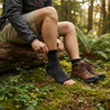 Person sitting on a log in a forest, wearing black ankle support brace and brown hiking boots.