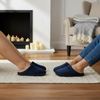 Two pairs of feet wearing navy blue slippers on a rug in a living room.